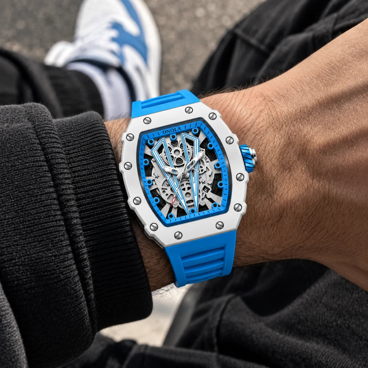 Blue tonneau skeleton watch with silicone strap worn on a men's wrist